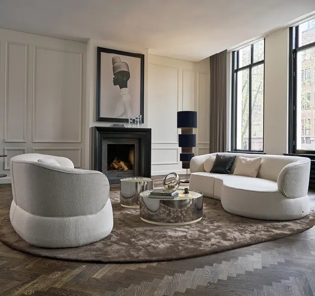 Helle Wohnzimmereinrichtung mit runden Stoffsofas und einem schwarzen Kamin im Hintergrund